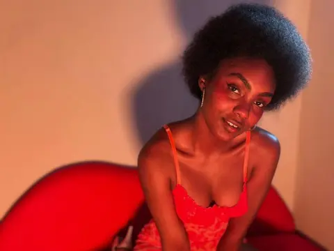 Asha_zuri69 wearing a red lace camisole, posing with her hair in an afro while sitting on a red sofa.