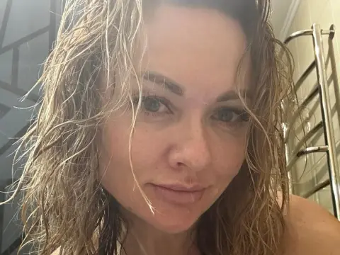 Close-up portrait of a woman with wet blonde hair in a bathroom setting with a natural, serene mood.