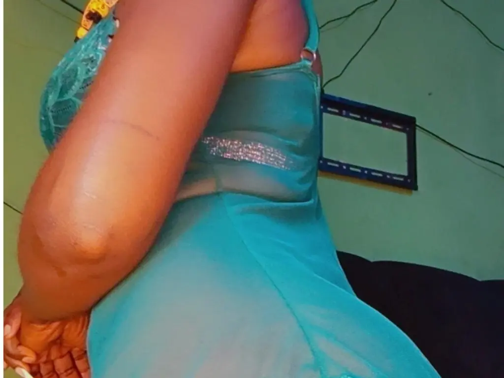 Olivialips696 wears a light blue lace camisole while posing in a room with a green wall and a black frame behind her.