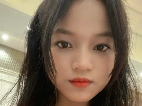 BabySweet18x — Close-up portrait of a young woman with long dark hair and red lipstick in a bright indoor setting.