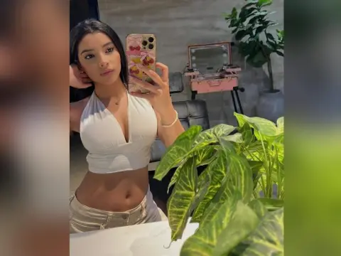 Young woman in a white crop top taking a mirror selfie in a modern room with green plants.