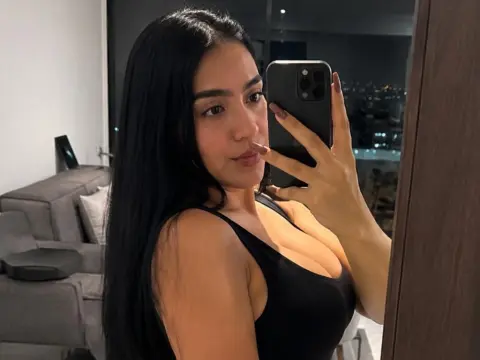 Young woman with long dark hair in a black tank top taking a selfie in a modern apartment at night.
