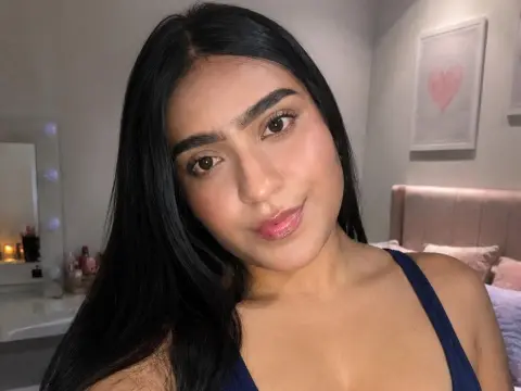 Young woman with long dark hair wearing a navy blue tank top in a cozy bedroom setting.