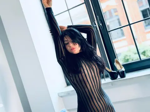 Woman in a black sheer striped bodysuit stretching by a bright window in a modern room.