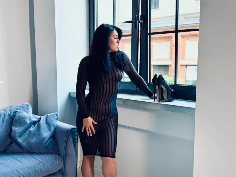 Elegant woman in a black sheer striped dress standing by a window in a bright modern living room.