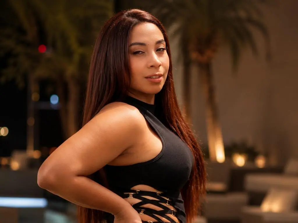 Confident woman in a black cutout mini dress posing on a rooftop terrace at night with city lights.