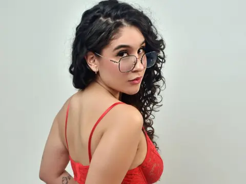 Young woman with curly dark hair wearing red lace lingerie and glasses in a studio setting.