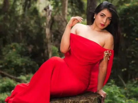 Elegant woman in a flowing red off-the-shoulder gown sitting peacefully in a lush green forest setting.