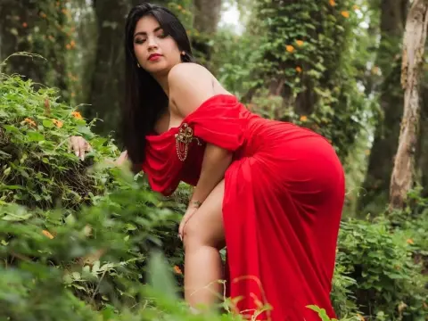 Elegant woman in a flowing red dress posing amidst lush green forest foliage in a romantic mood.