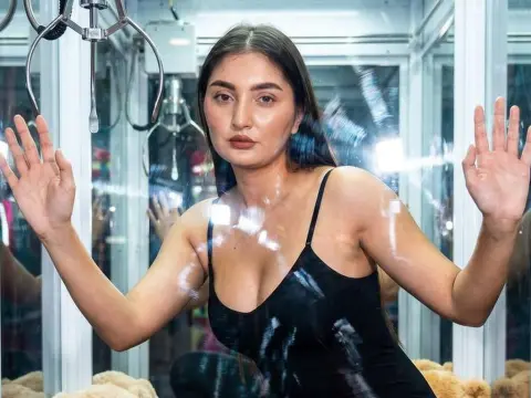 AzzaLeeX poses with her hands pressed against the glass, wearing a black camisole top with her long dark hair down.