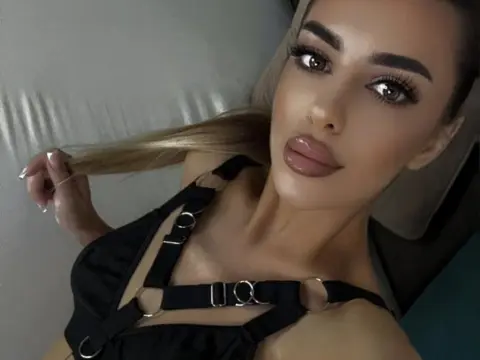 IvyLust poses close-up, wearing a black strap-detail top while holding a strand of her long blonde hair.
