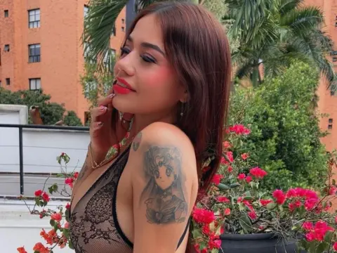 DarkHoneeey poses outdoors in a black lace bodysuit, showing off her long brown hair and anime shoulder tattoo near red flowers.