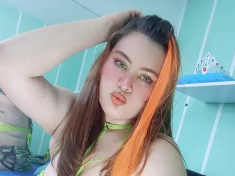 Young woman with orange hair highlights in a lime green bikini posing in a bright teal room.