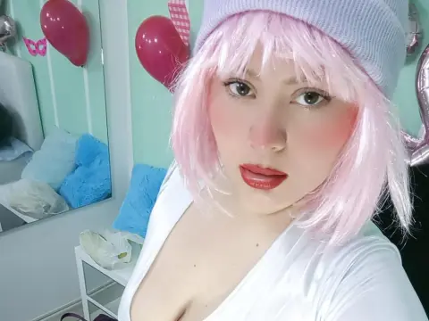 Woman with pink hair and white top posing in a room with pink balloons and a dreamy aesthetic.