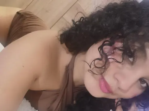 Young woman with curly dark hair wearing a brown halter top relaxing in a cozy indoor setting.