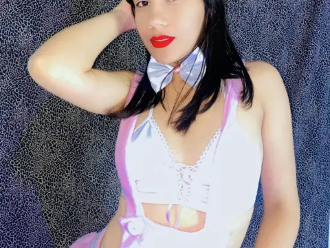 Zoee_Smith wears a white satin corset with a white bow tie and black hair, posing against a dark textured background.