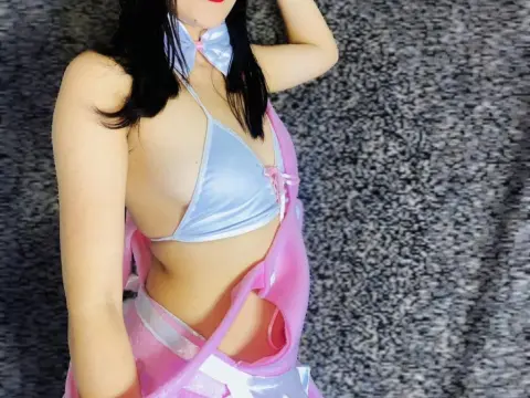 Zoee_Smith poses in a light blue satin bikini top and pink skirt against a grey textured wall.