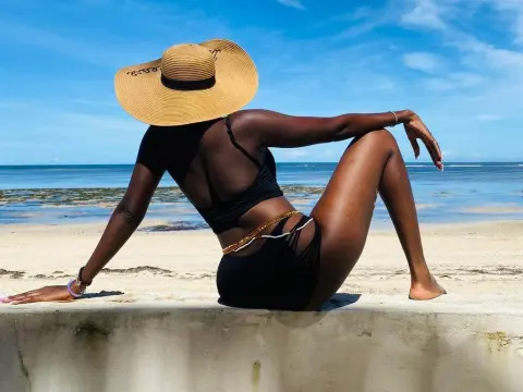 Darkmajestiy — Black woman in black bikini and straw sun hat relaxing on a sunny tropical beach.