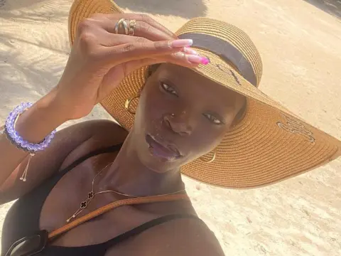 Darkmajestiy — Stylish Black woman in a black bikini and wide-brimmed straw hat relaxing on a sunny beach.