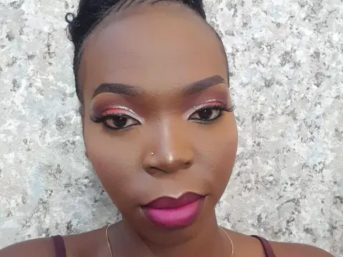 Darkmajestiy — Black woman with glamorous pink eyeshadow and bold berry lipstick posing against a textured grey wall.