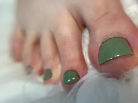 A close-up shot of SophiaNoire's toes with green nail polish resting on white faux fur.
