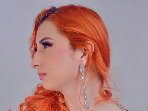 VenusMontiel shows off her bright orange hair and long silver earrings while looking off-camera against a plain light background.
