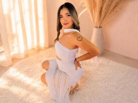 Smiling woman in a white cutout dress sitting on a fluffy rug in a bright, sunlit room.