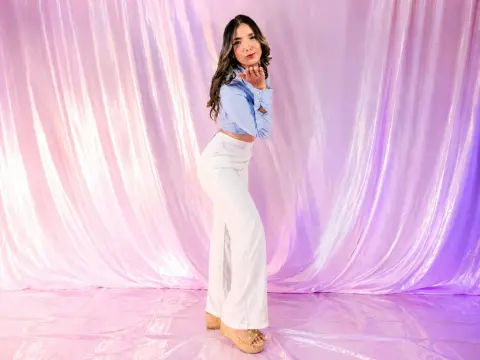 Stylish woman in a light blue blouse and white wide-leg trousers posing against a shimmering pink backdrop.