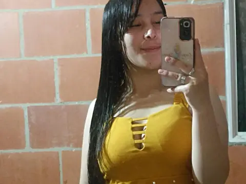 AlairaAura takes a mirror selfie wearing a yellow sleeveless top with a cutout detail, showing her long dark hair against a brick wall.