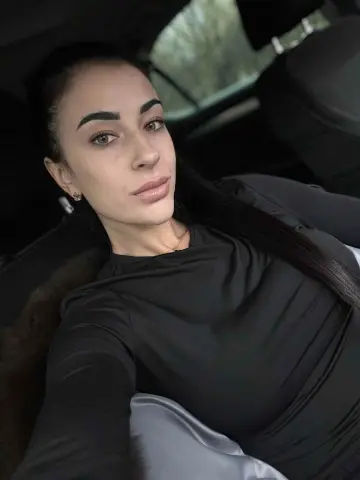 Karinabrunette — Karinabrunette poses in a black long-sleeve shirt with her long dark hair down while sitting in a car.