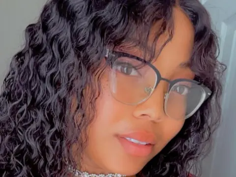 GiveCaramelKiss shows off her long, wavy black hair and glasses in a close-up headshot.