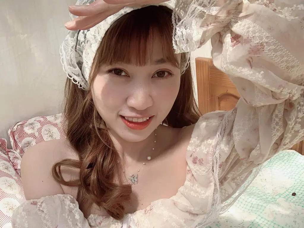 Mayle0234 smiles while wearing a white lace floral top and a matching lace headwrap, showing her shoulders and long brown hair.