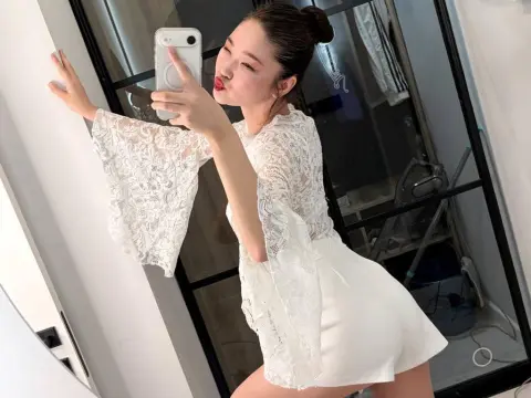 veryhotasiangirl1 poses for a mirror selfie wearing a white lace long-sleeve top and white shorts.