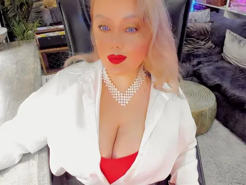 ListenEtername — Blonde woman in a white shirt and pearl necklace sitting in a cozy living room with a glamorous mood.