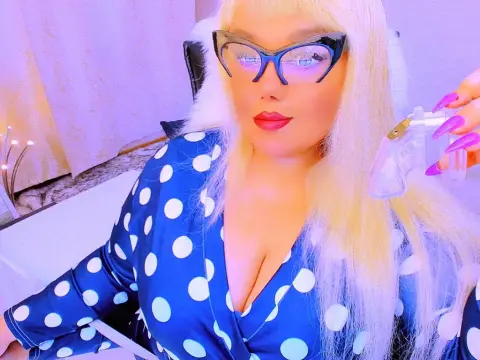 ListenEtername — Blonde woman in blue polka dot dress and black cat-eye glasses posing in soft purple lighting.