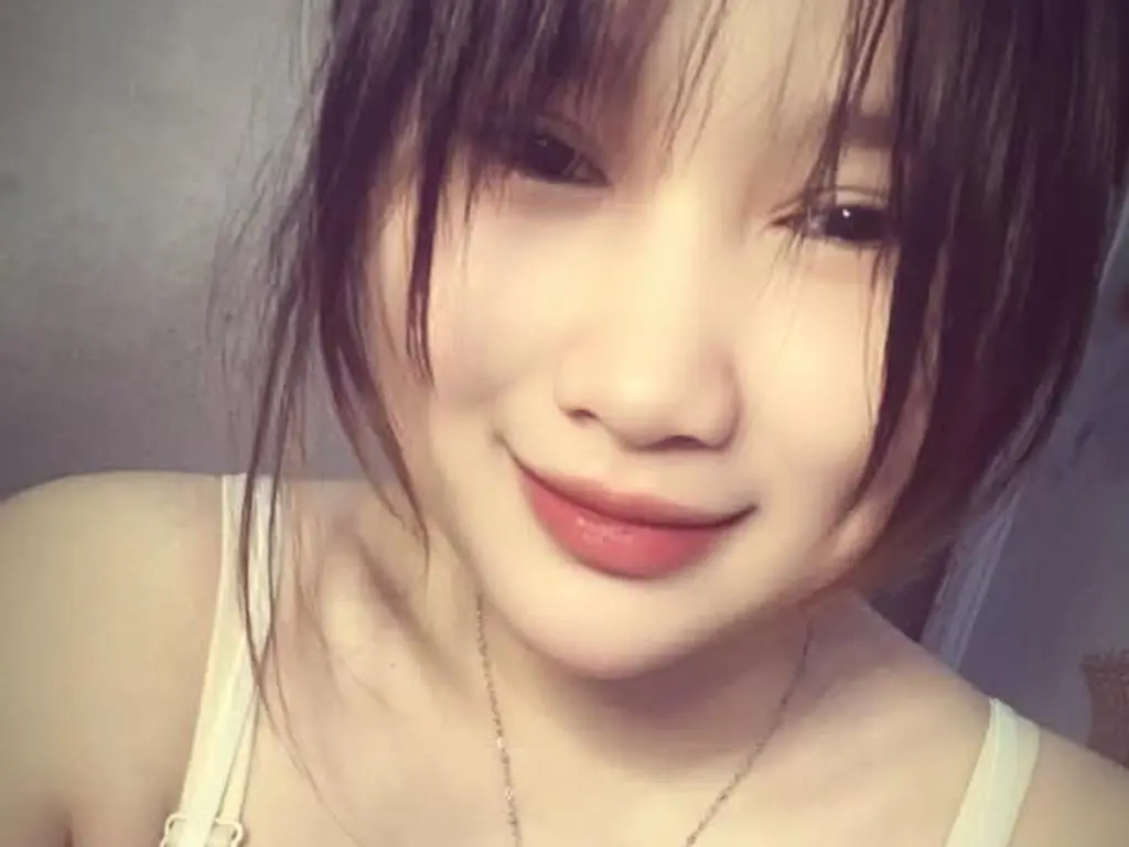 Nuribby smiles at the camera with long dark hair and a thin necklace, wearing a white tank top strap visible on her shoulder.