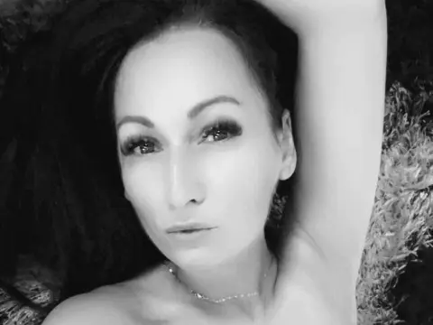 JazyBrowni poses with her arm up, showing her face, long dark hair, and a thin necklace in this black and white close-up.