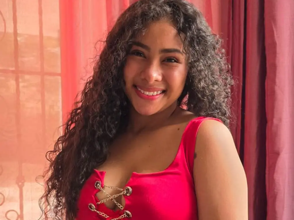 Luciatoloza1 smiling in a red lace-up top with her long curly hair flowing over her shoulders.