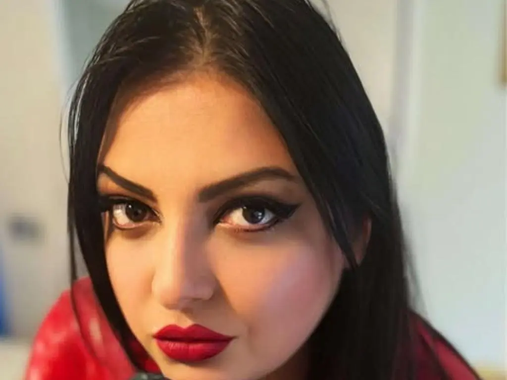 QueenMandy looks directly at the camera with long black hair and bold red lipstick.