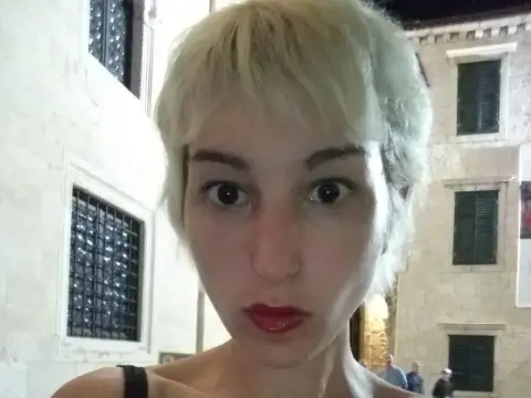 Blonde woman with red lipstick posing at night in a historic European stone street setting.