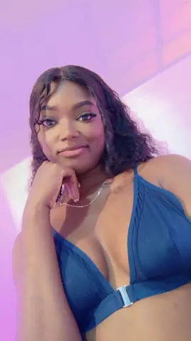KeisyCollinss — KeisyCollinss poses with her hand under her chin, wearing a blue bikini top and a silver necklace against a soft pink background.