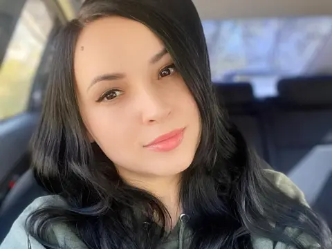 Smiling young woman with long dark hair wearing a green hoodie inside a car on a bright day.