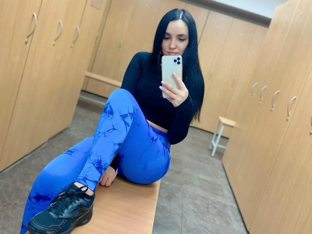 AmelyAngelx — Young woman in blue patterned leggings and black long-sleeve top taking a selfie in a gym locker room.
