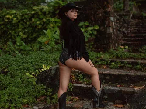 AmelyAngelx — Woman in black fringe top and sparkly shorts posing in a lush green forest setting.