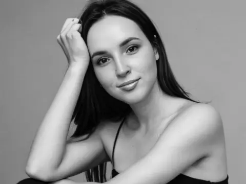 AmelyAngelx — Portrait of a smiling young woman with long dark hair wearing a black top against a plain gray background.