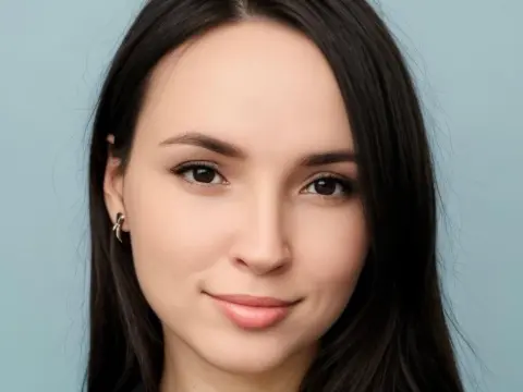 AmelyAngelx — Close-up portrait of a smiling young woman with long dark hair against a light blue background.