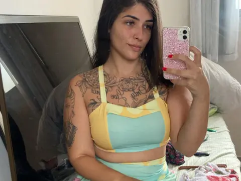 tali_majid takes a mirror selfie wearing a yellow and mint green crop top, showing off her many tattoos.