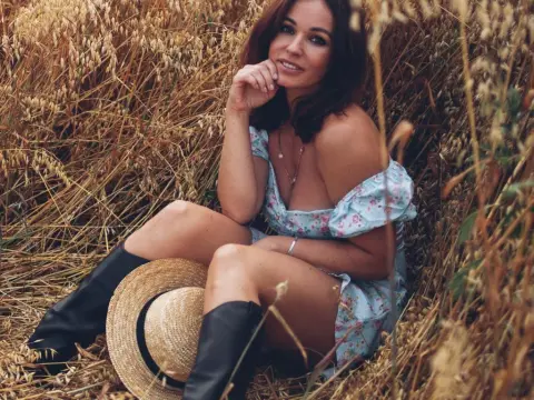 BestHottieEver — Smiling woman in a blue floral sundress and black boots sitting in a golden wheat field during sunset.