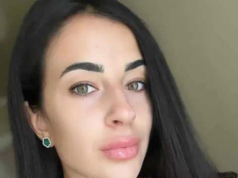 Karinabrunette — Karinabrunette looks directly at the camera with her long, straight black hair and light eyes, wearing small green earrings.