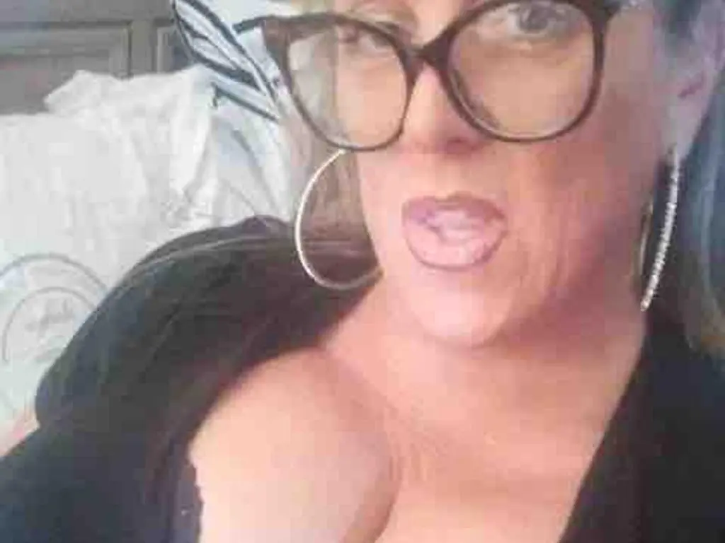 BBWgoDDDess wears black glasses and a black top while looking into the camera with her mouth slightly open.